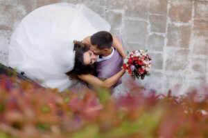 Bride and groom embrace and kiss, wedding dress spilling around them with a bouquet visible nearby.