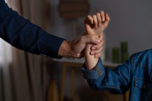Adult hand firmly gripping a child’s wrist indoors, showing a restraining grip on the forearm.
