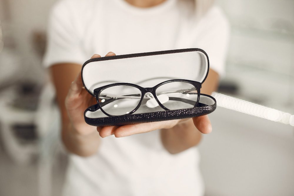 776630 - All Visión - Europa Love 24h Black-rimmed eyeglasses held in an open black case toward the camera by a person in a white shirt.
