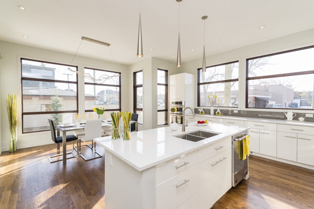 Bright white kitchen with island sink, stainless appliances, and large windows; yellow flower vases on the island.