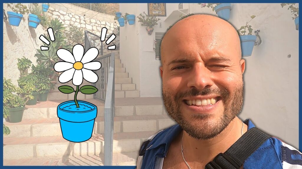 Smiling man taking a selfie beside a large cartoon daisy in a blue pot on a sunlit stone staircase.